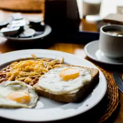 Un petit déjeuner sportif : œufs au plat, haricots et fromage râpé sur une assiette blanche, avec une tasse de café à côté.