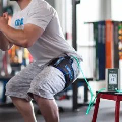 Un athlète en plein squat, équipé d'un appareil de bfr kiné à la cuisse, mesure ses performances.