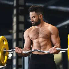 Un homme musclé s'entraîne avec une barre chargée de poids jaunes, concentré sur sa prise de masse.