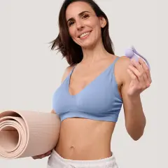 Une femme souriante tient un tapis de yoga et un accessoire pour la musculation du périnée, suggérant quels sont les sports favorables à la musculation du périnée.