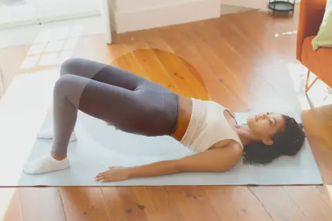 Femme en tenue de sport effectuant un pont sur un tapis, une posture idéale pour muscler son périnée et renforcer son corps.