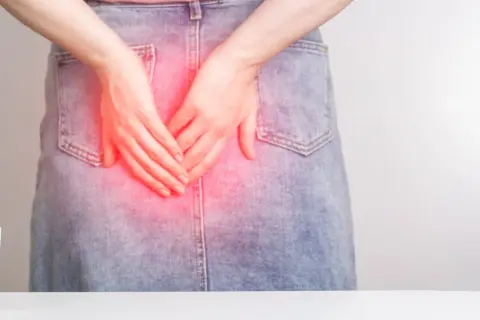Main tenant ses mains sur sa zone anale, une zone rouge indique une douleur. Apprendre comment relâcher le sphincter anal peut soulager l'inconfort.