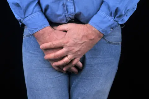 Homme aux mains croisées sur le devant, possiblement pour soulager une vessie hyperactive. L'électrostimulation peut aider.