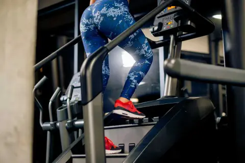 Femme en legging bleu sur un stepper, travaillant ses abdos fessiers. Entraînement intense pour sculpter son corps.