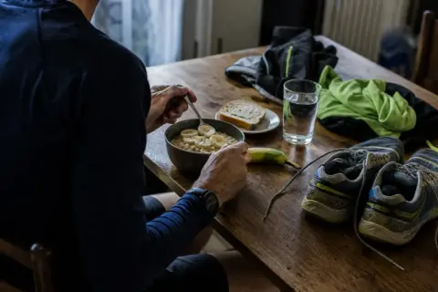 Préparation pour un semi-marathon : un bol de flocons d'avoine aux bananes, une tranche de pain, une banane, une verre d'eau, des chaussures de course et des vêtements.