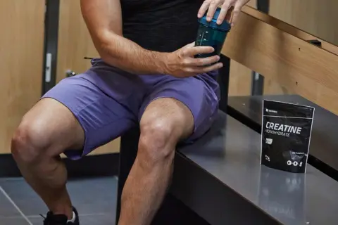 Un homme prépare sa boisson post-entraînement avec de la créatine. Elle sert à améliorer la performance et la récupération musculaire.