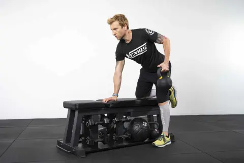 Homme effectuant un exercice de tirage avec kettlebell sur un banc de musculation.