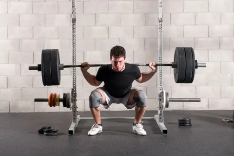Un homme concentré effectue un back squat, la barre chargée reposant sur ses épaules, dans une salle de sport.