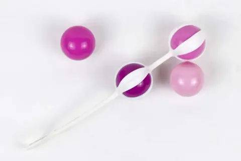 Trois boules de geisha, deux roses et une violette, sur fond blanc.