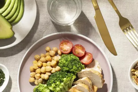 Assiette de poulet, brocolis, pois chiches et tomates, avec avocat et noix. Un repas équilibré pour un rééquilibrage alimentaire réussi.