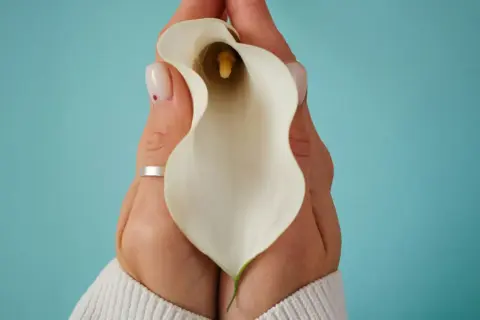 Mains tenant une calla blanche, évoquant la délicatesse et la guérison après une douleur périnée après accouchement.