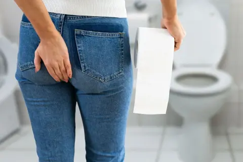 Femme tenant du papier toilette, main sur la fesse, suggérant l'incontinence anale. Recherche d'un traitement naturel.
