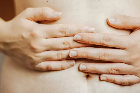Mains d'une femme sur son ventre, évoquant la constipation et la pression sur la vessie.