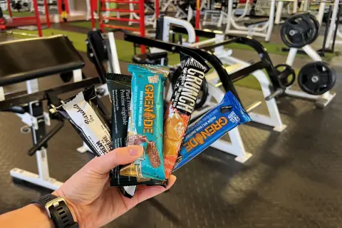 Une main tient plusieurs barres protéinées, parfaites comme collation avant ou après le sport, dans une salle de sport.