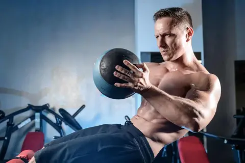 Homme musclé effectuant un exercice oblique avec un medecine ball, concentré sur son entraînement.