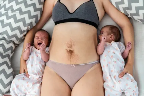 Maman avec ses jumeaux, le ventre marqué par la grossesse, évoquant la pesanteur périnée après accouchement.