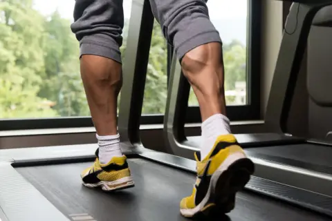 Jambes musclées sur un tapis roulant, mettant en valeur l'exercice mollet.
