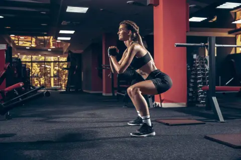 Femme en tenue de sport effectuant un squat dans une salle de sport. Elle est concentrée sur son exercice de squat sport.
