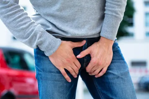 Un homme tient ses mains sur son entrejambe, suggérant une douleur pelvienne.