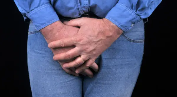 Homme aux mains croisées sur le devant, possiblement pour soulager une vessie hyperactive. L'électrostimulation peut aider.