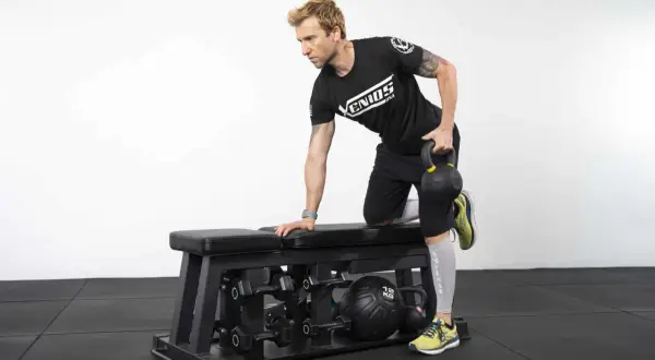 Homme effectuant un exercice de tirage avec kettlebell sur un banc de musculation.