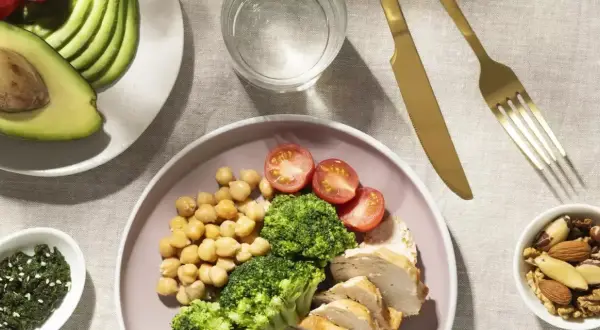 Assiette de poulet, brocolis, pois chiches et tomates, avec avocat et noix. Un repas équilibré pour un rééquilibrage alimentaire réussi.