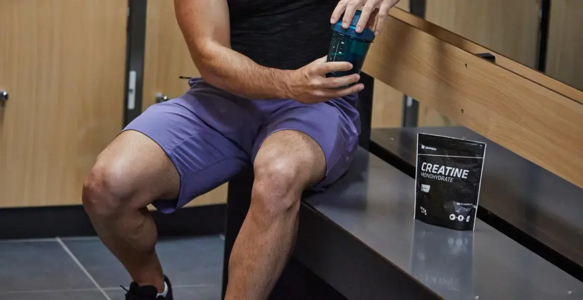 Un homme prépare sa boisson post-entraînement avec de la créatine. Elle sert à améliorer la performance et la récupération musculaire.