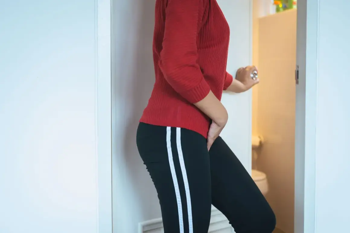Femme tenant son bas-ventre, porte ouverte sur des toilettes. Elle ressent une envie fréquente d'uriner sans infection urinaire.