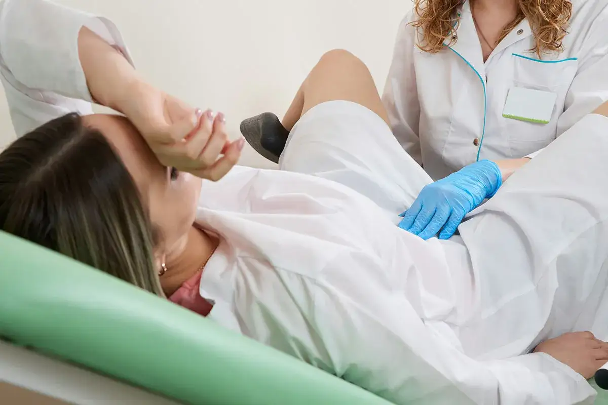 Une patiente en position gynécologique, examinée par une kiné ou une sage-femme pour une rééducation périnéale.