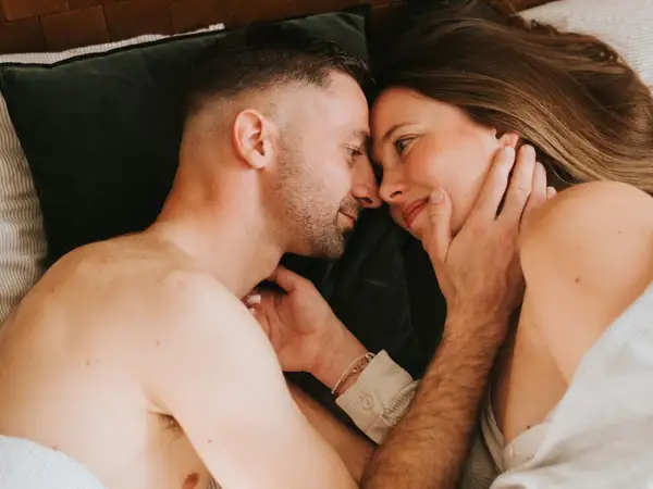 Un couple se regarde tendrement au lit. Ils semblent se retrouver après une période difficile, peut-être après une naissance et une épisiotomie, redécouvrant l'intimité.