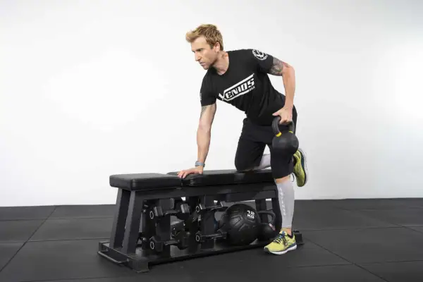 Homme effectuant un exercice de tirage avec kettlebell sur un banc de musculation.
