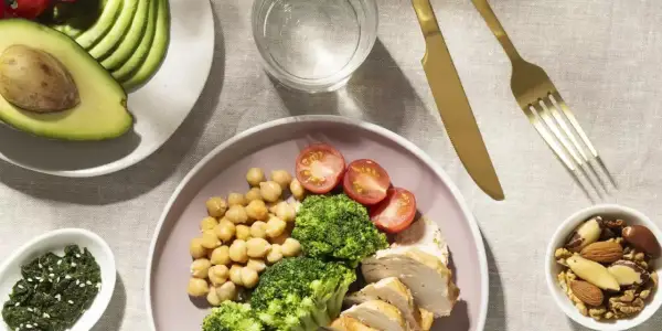 Assiette de poulet, brocolis, pois chiches et tomates, avec avocat et noix. Un repas équilibré pour un rééquilibrage alimentaire réussi.