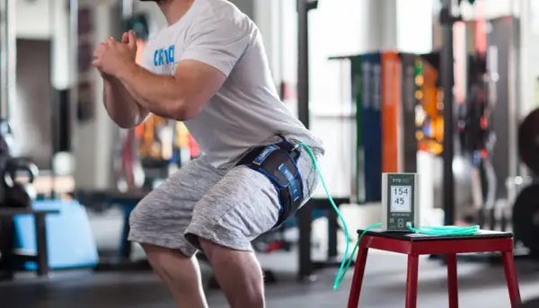 Un athlète en plein squat, équipé d'un appareil de bfr kiné à la cuisse, mesure ses performances.