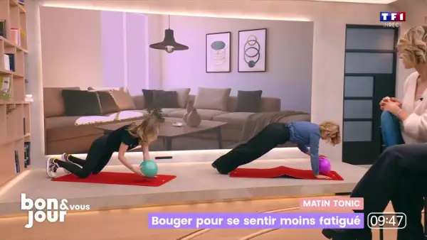 Deux femmes font des exercices sur des tapis rouges. L'une d'elles tient un ballon vert, l'autre un ballon violet. Elles semblent faire du sport tous les jours pour rester en forme.