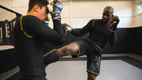 Deux athlètes s'entraînent en mma sport de combat. L'un porte des protège-tibias et donne un coup de pied, l'autre se protège la tête.