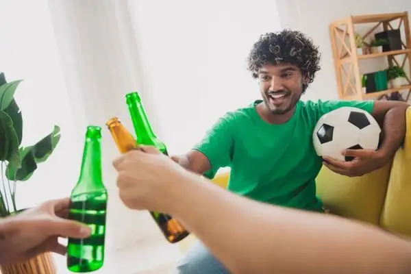 Un homme souriant avec un ballon de foot trinque avec des bières, une récompense parfaite après le sport.